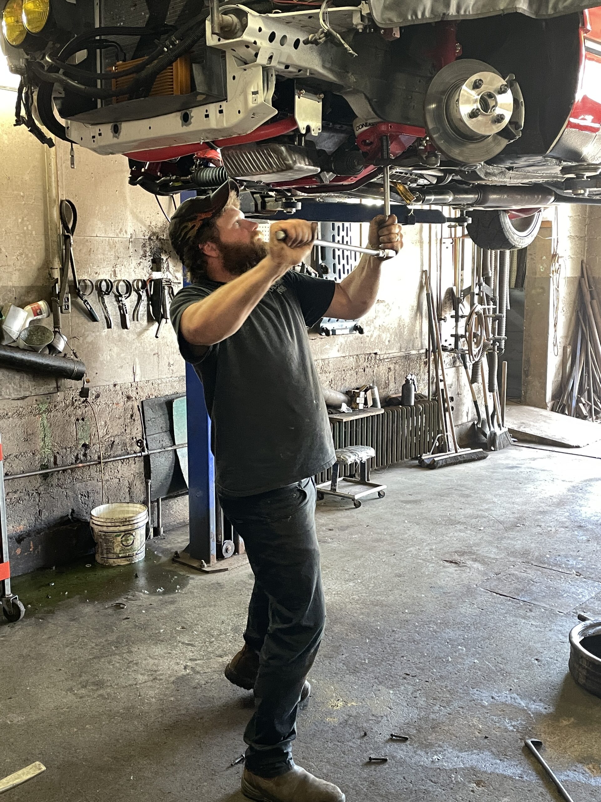 Tyler from Lawrencetown Motors uses a crank shaft on the underside of a car on a lift.